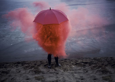 Person with umbrella standing amidst smoke while standing at beach 