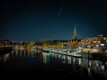 Illuminated buildings by river against sky at night