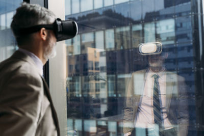 Mature businessman wearing virtual reality simulator standing in front of window