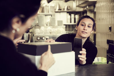 Owner with phone while coworker pointing at modem box in cafe
