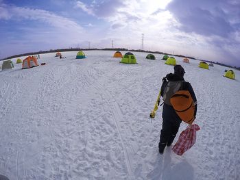 Rear view of person walking on snow covered land against sky