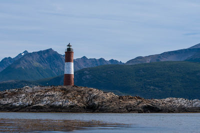 Lighthouse by sea and mountain against sky