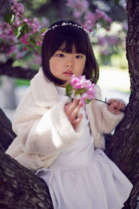 Korean girl in a white light fur coat and a headband sitting on a tree branch in a garden