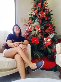 Young woman sitting by christmas tree at home