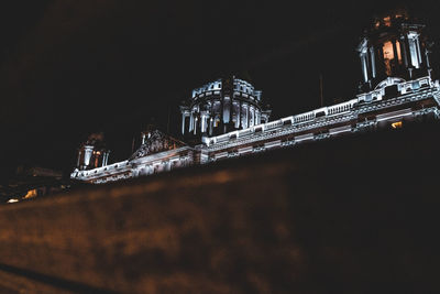 Low angle view of illuminated bridge against buildings at night