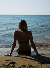 Rear view of woman sitting on beach against sky