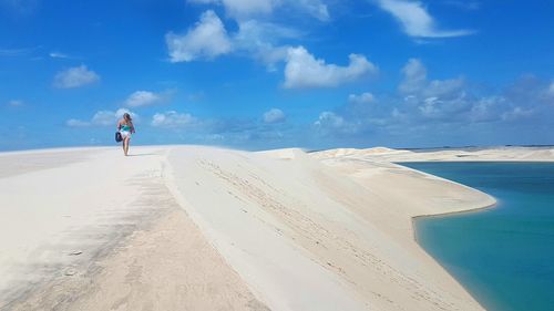 Rear view of woman walking on beach against sky