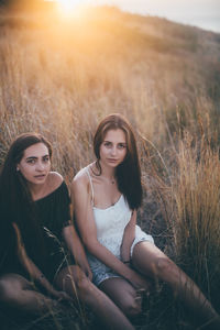 Female friends sitting on land against sky during sunset