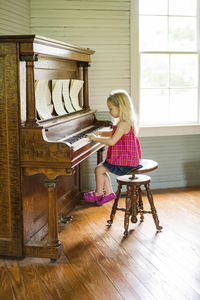 Side view of girl playing piano while sitting on stool at home