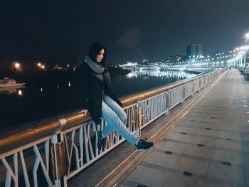 Portrait of woman sitting on railing in city at night