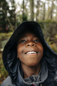 Thoughtful boy looking away wearing raincoat in forest