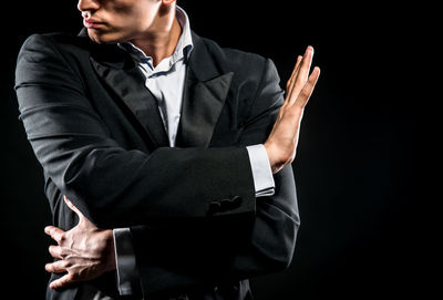 Midsection of man in blazer gesturing against black background