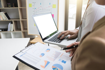 Midsection of colleagues discussing over graph in office