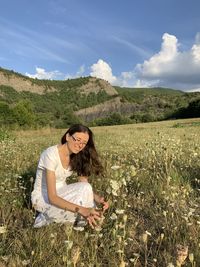 Smiling woman crouching amidst plants on land against sky
