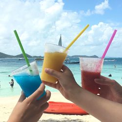 Cropped image of hands holding drink at beach against sky