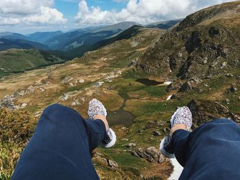 Low section of person sitting on mountain against sky