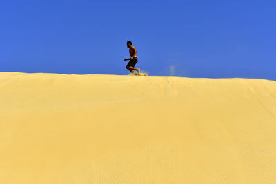 Man on sand dune in desert against clear blue sky