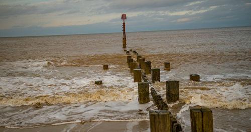 Wooden posts on beach against sky