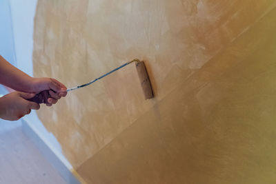 Roller painting the wall with gold colour against white wall near the fuse.