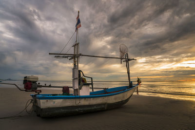 Boat moored on beach against sky during sunset