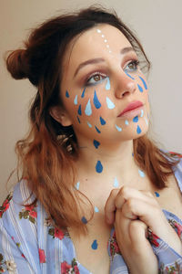Close-up of thoughtful young woman with painted face against beige background