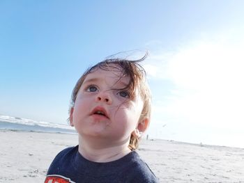 Close-up of boy looking up at beach against sky