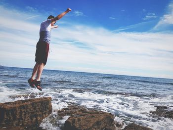 Full length of woman standing on rock at beach against sky