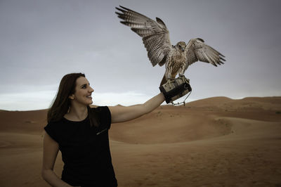 Woman with bird standing at desert against sky