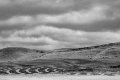 Tire tracks on sand dune against sky