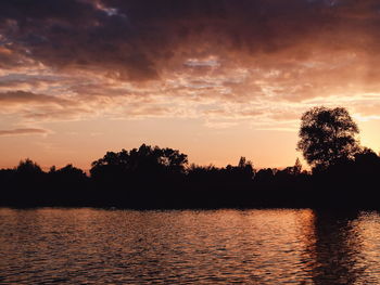 Silhouette trees by lake against sky during sunset