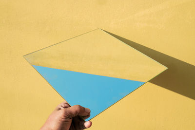 Low section of person holding paper against yellow wall
