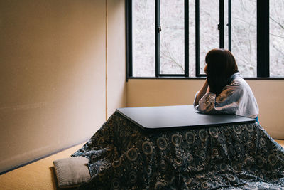 Side view of woman by table in room at home