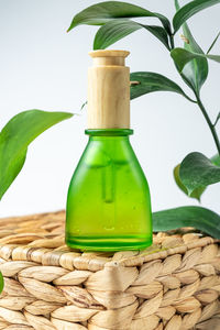 Green frosted cosmetic bottle with pipette on wooden podium, product packaging with natural ruscus