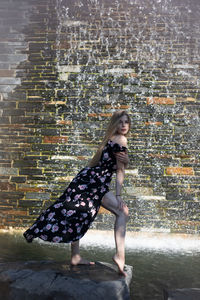 Full length of young woman standing against brick wall