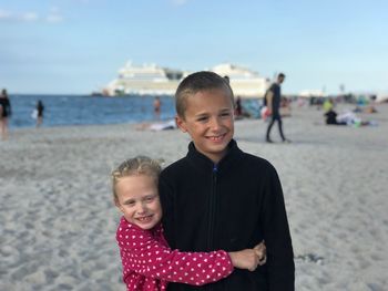 Happy siblings standing on sand at beach