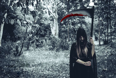 Woman wearing grime reaper costume while standing in forest