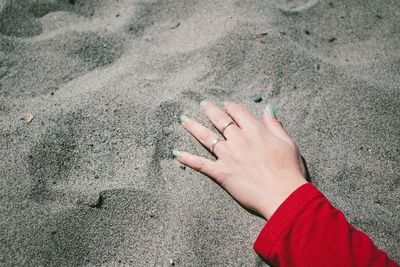 High angle view of woman hand on sand at beach during sunny day