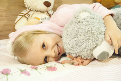 Portrait of smiling girl gesturing peace sign while holding teddy bear on bed at home