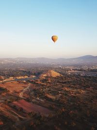 Hot air balloon flying over landscape and ancient pyramid against sky