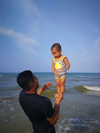 Full length of father and daughter on beach against sky