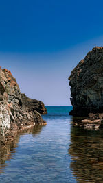 Rock formations in sea against clear blue sky