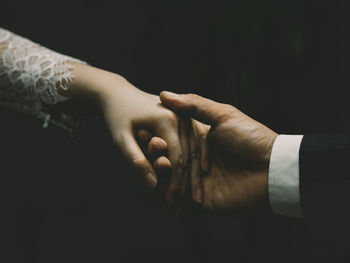 Close-up of couple holding hands over black background