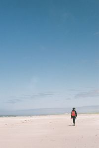 Woman walking at beach against blue sky