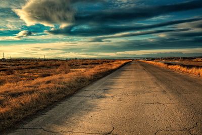 Dirt road amidst field against sky during sunset