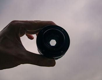 Close-up of hand holding camera lens against sky