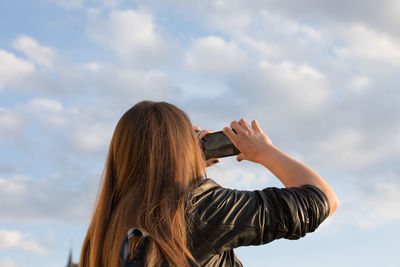 Portrait of woman photographing against sky