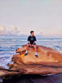 Rear view of woman sitting at beach against sky