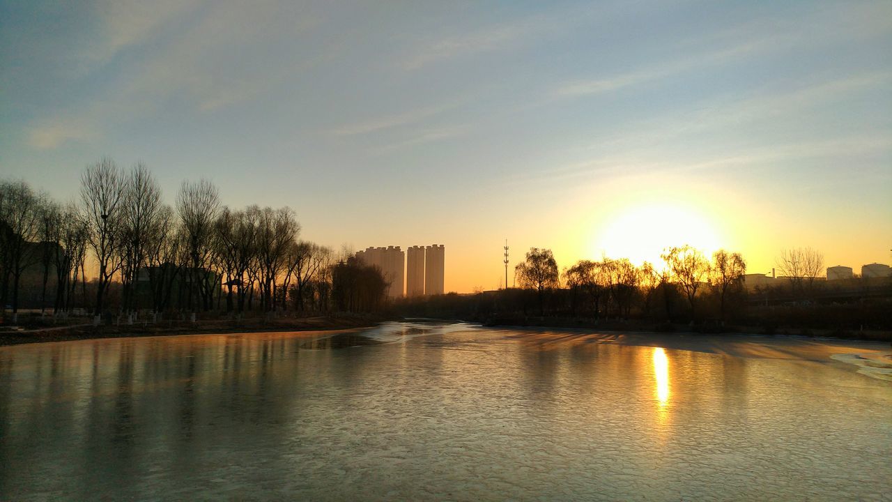 sunset, water, reflection, sun, sky, sunlight, waterfront, building exterior, beauty in nature, nature, architecture, outdoors, scenics, no people, tree, cloud - sky, built structure, travel destinations, skyscraper, city, urban skyline, cityscape, day