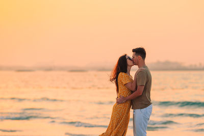 Rear view of couple standing at sea during sunset