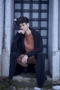 Portrait of young man sitting against door